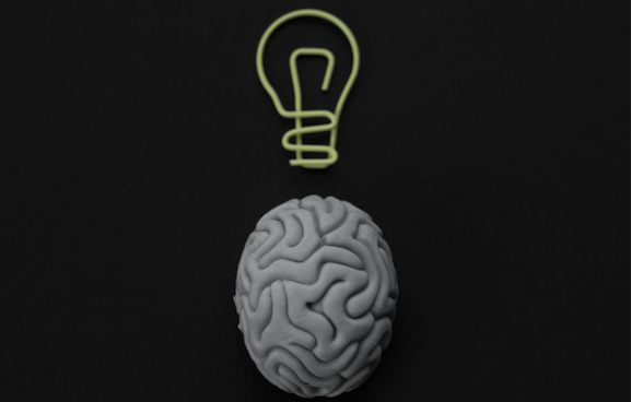Gray brain with lightbulb on a black background.