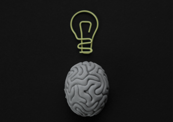 Gray brain with lightbulb on a black background.