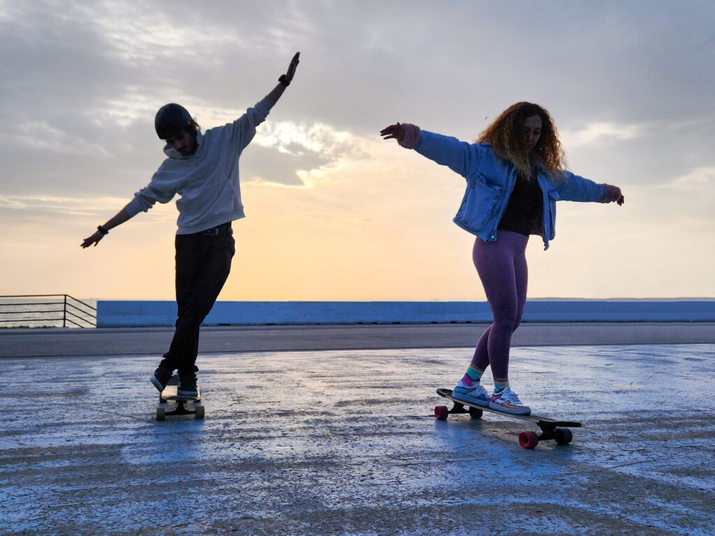 Woman and man skateboarding on a rooftop during sunset