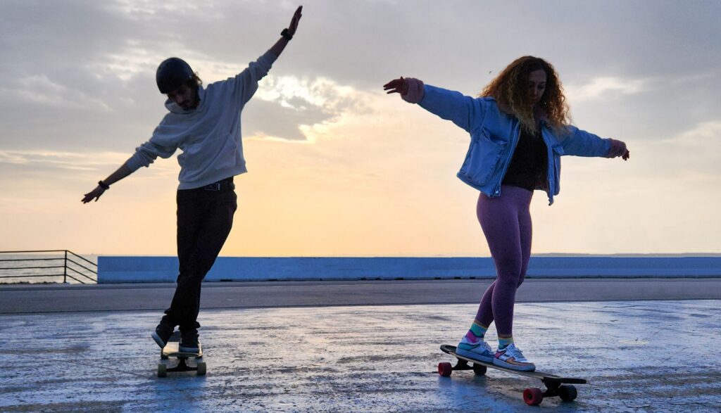 Woman and man skateboarding on a rooftop during sunset